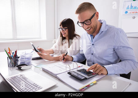 Two Young Businesspeople Calculating Invoice With Calculator Stock Photo