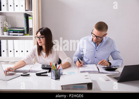 Two Young Businesspeople Calculating Invoice With Calculator Stock Photo