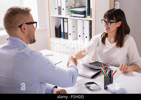 Smiling Client Shaking Hand With  Financial Advisor Over Desk At Workplace Stock Photo