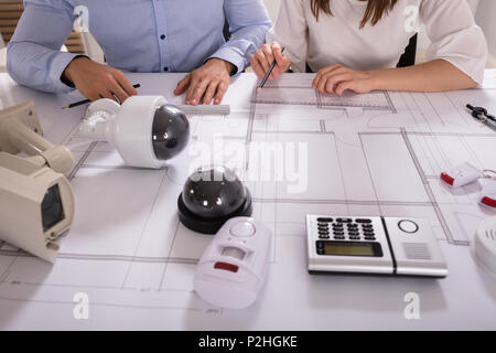 Various Security Equipments In Front Of Two Architects Planning Project On Blueprint Stock Photo