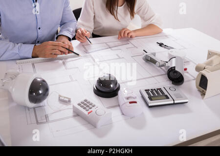 Various Security Equipments In Front Of Two Architects Planning Project On Blueprint Stock Photo
