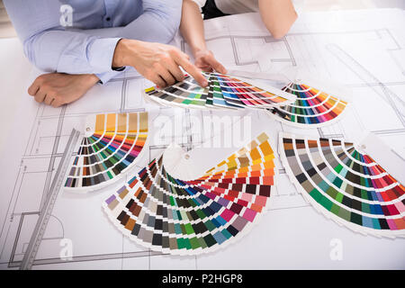 Close-up Of Two Architect's Hand Choosing Color From Various Colorful Swatches While Working On Blueprint Stock Photo