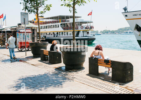 Istanbul, June 17, 2017: People sit on benches and rest on the shores of the Bosphorus. Nearby ferries and passenger ships. Ordinary city life. Stock Photo