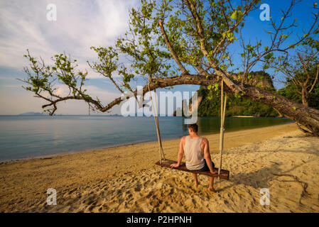 Young boy sits on a swing on Ko Hong island in Thailand Stock Photo