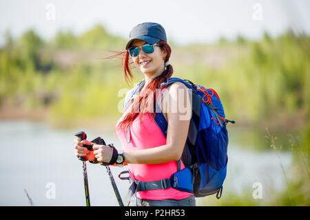 Image of sports woman with walking sticks and backpack on background of lake and vegetation Stock Photo