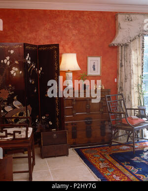 Antique inlaid screen beside lighted lamp on chest-of-drawers in red study Stock Photo