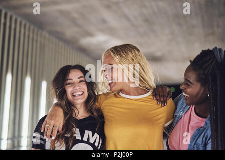 Three young girlfriends walking together down a walkway in the city at night laughing and having fun Stock Photo