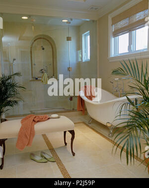 Cream upholstered stool and slipper bath in modern bathroom with glass doors on large walk-in shower cabinet Stock Photo