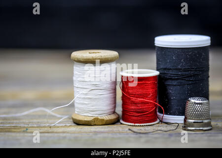 Sewing thread black , white and red with a thimble beautifully folded on a wooden background Stock Photo