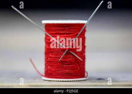 Sewing thread red with two needles closeup on wooden background Stock Photo