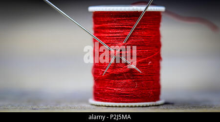 Sewing thread red with two needles closeup on wooden background Stock Photo