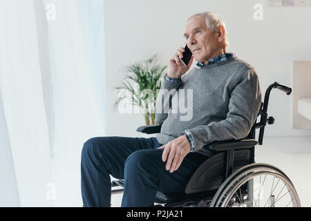 Senior man in wheelchair making a phone call in empty room Stock Photo