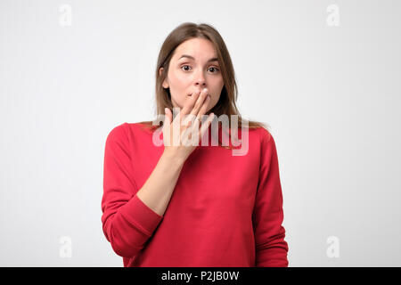 Close up portrait of attractive, charming, woman in red pulover closing her mouth with fingers. She is worried. She can't say anything. Getting bad ne Stock Photo