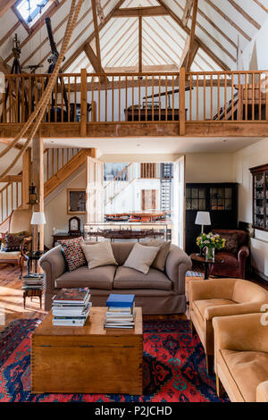 Double height living room with antique telescopes on wooden mezzanine with suede armchairs in Sussex barn conversion Stock Photo