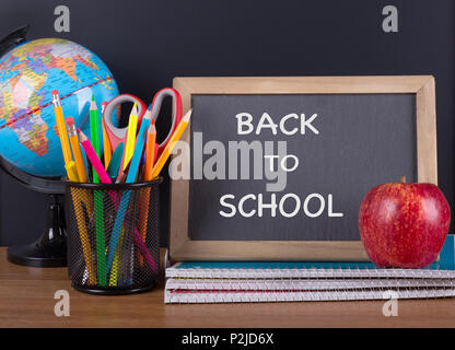 School accessories and a chalkboard with "Back To School" text on a wooden desktop and a black background Stock Photo
