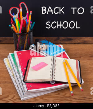 School notebooks with pencils on a wooden desktop with BACK TO SCOOL written on a blackboard in background Stock Photo