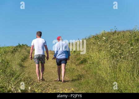 Holidaymakers walking along a footpath through a field on West Pentire in Newquay in Cornwall. Stock Photo