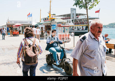 Istanbul, June 17, 2017: A guy or a young man is driving down the city street on an electric scooter or bike. Nearby are the locals on their own busin Stock Photo