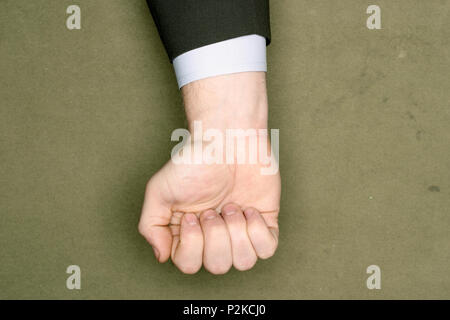 Businessman in a suit clenching his hand to make a fist in a cropped view over a neutral green brown background with copy space Stock Photo
