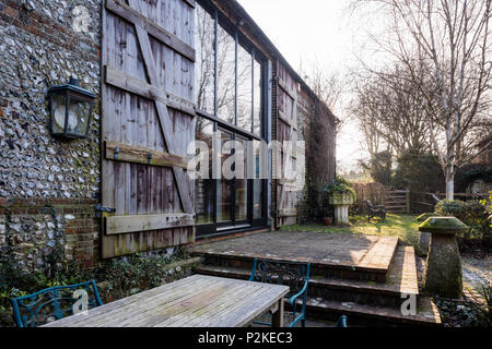 Outdoor furniture on terrace of barn convesrion with large windows and timber shutters, Sussex Stock Photo