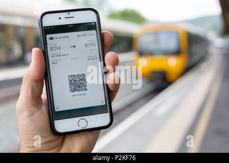 BATH, UK - 15 JUNE, 2018 : Close-up of an iPhone 6 screen displaying an electronic train ticket, with a train at the station platform behind Stock Photo