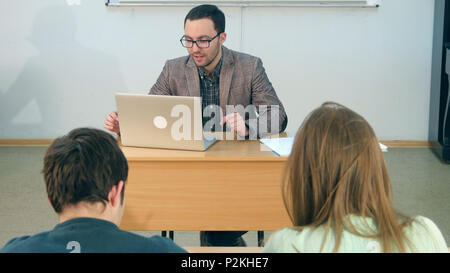 Happy teacher with laptop giving lesson to a class Stock Photo