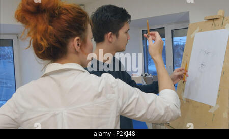 Female artist teaching young man to draw with pencil Stock Photo