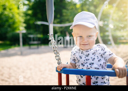 Baby boy playing in playground area. Portrait of smiling toddler looking away with happy face, having fun. Swaying on sunny summer day outdoors. Stock Photo