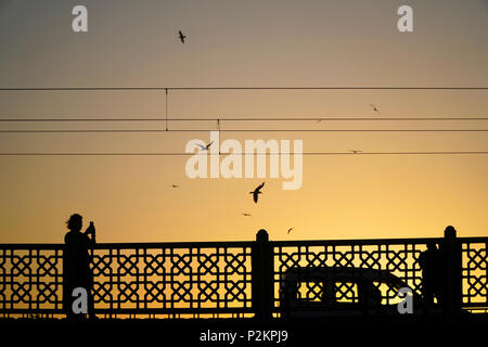 Istanbul, Turkey - June 12, 2018 : Silhouettes of some people with a car on The Galata Bridge at Istanbul. A woman is taking mobile photo. Stock Photo