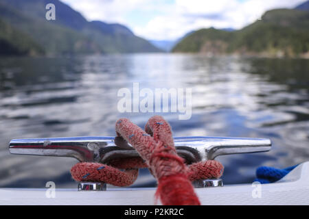 View from rear of boat with cleat and rope looking over beautiful clear ocean water and coastal shoreline. Stock Photo