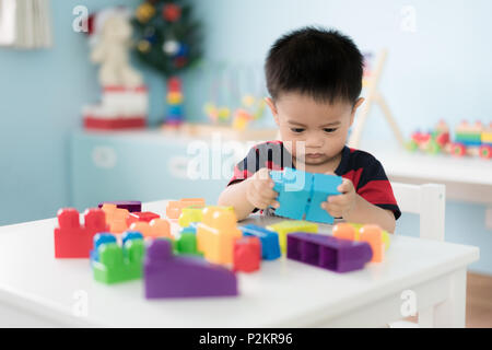 Adorable Asian Toddler baby boy sitting on chair and playing with color block toys at home. Stock Photo