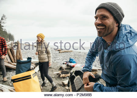 Smiling man enjoying weekend surfing getaway with friends on rugged beach