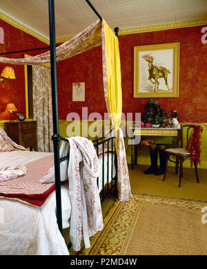 Pink+white bathrobe on black metal four-poster bed with Toile-de-Jouy drapes in red French bedroom Stock Photo