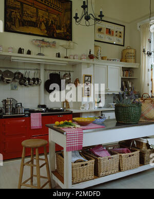 Storage baskets on low shelf on island unit with stainless steel worktop in country kitchen with red double Aga Stock Photo