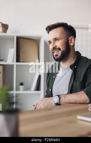 Handsome bearded man smiling and looking away in office Stock Photo