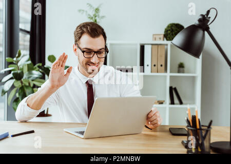 handsome smiling businessman waving and making video call on laptop Stock Photo