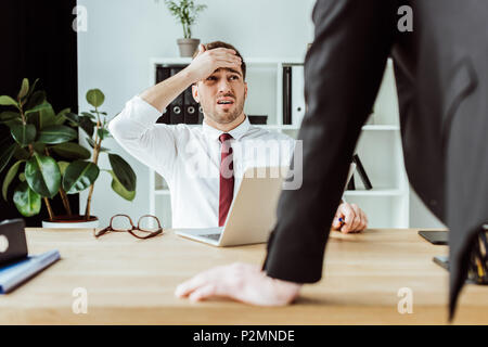 scared businessman with laptop looking at angry boss in office Stock Photo