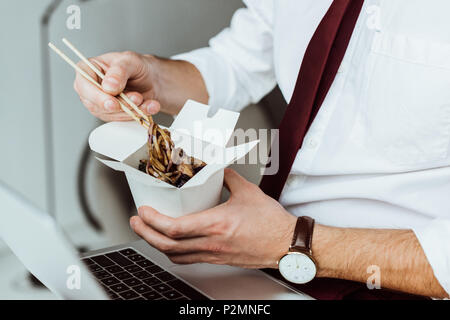 cropped view of businessman with laptop eating noodles in office Stock Photo