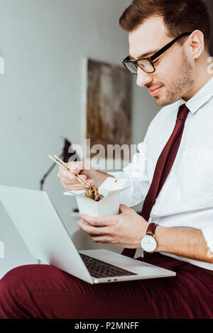 stylish businessman with laptop eating noodles in office Stock Photo