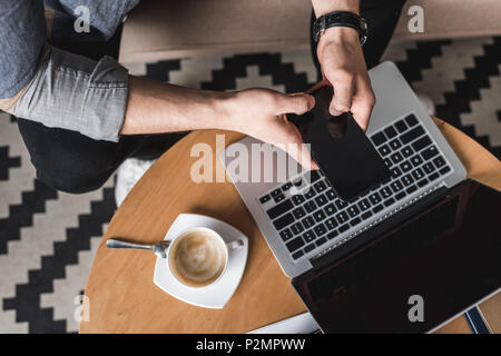 cropped shot fo man using smartphone with laptop on coffee table Stock Photo