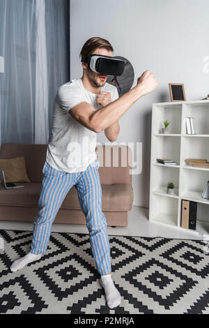 young man in virtual reality headset and pajamas playing fighting game Stock Photo