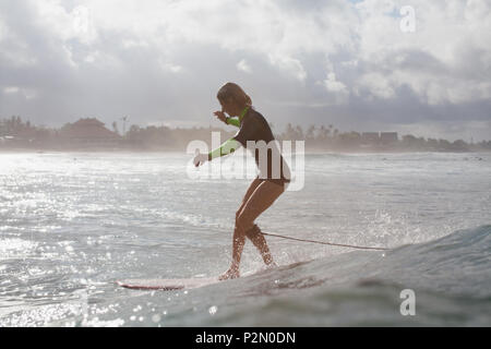 silhouette of sportswoman riding wave on surf board in ocean with backlit Stock Photo