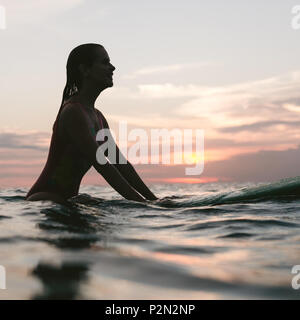 side view of silhouette of woman resting on surfing board in ocean