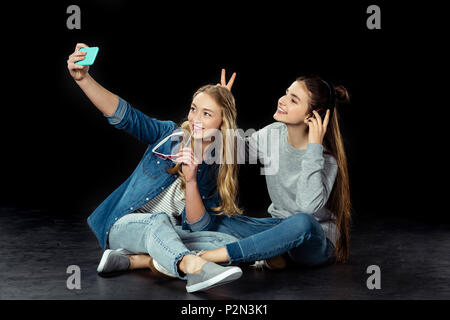 teen girls taking selfie while sitting on floor on black Stock Photo