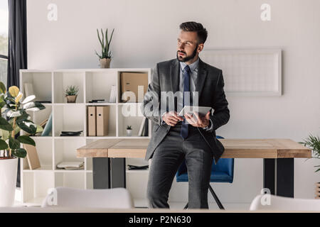 young bearded pensive businessman using digital tablet in modern office Stock Photo