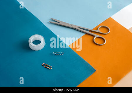 On colorful sheets of paper are scissors, paper clips, tape. Stock Photo
