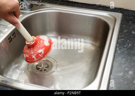 Man using a plunger with one hand and  water in sink, used to clean a clogged / blocked kitchen sink Stock Photo