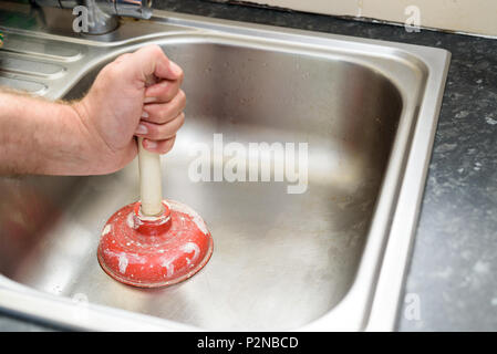 Man holding a plunger with one hand and no water in sink, used to clean a clogged / blocked kitchen sink Stock Photo