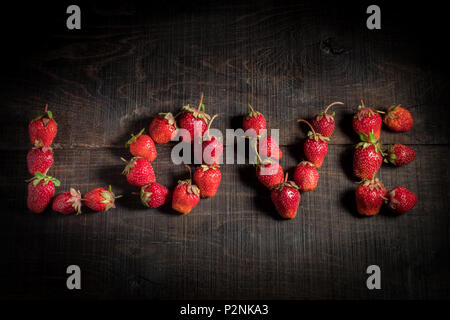 The word love is lined with strawberries. The inscription is love. Ripe strawberry fruit. Strawberries on a wooden background. Healthy food. Stock Photo