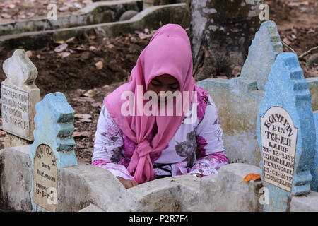 A woman seen praying next to a grave during the pilgrimage. Muslims seen with their relatives' grave during a pilgrimage at the public cemetery in Lhokseumawe City. Most Muslims in Aceh already made the last grave pilgrimage before entering the holy month of Ramadan and on the day of Eid al-Fitr, to pray for the families of those who have died. Stock Photo